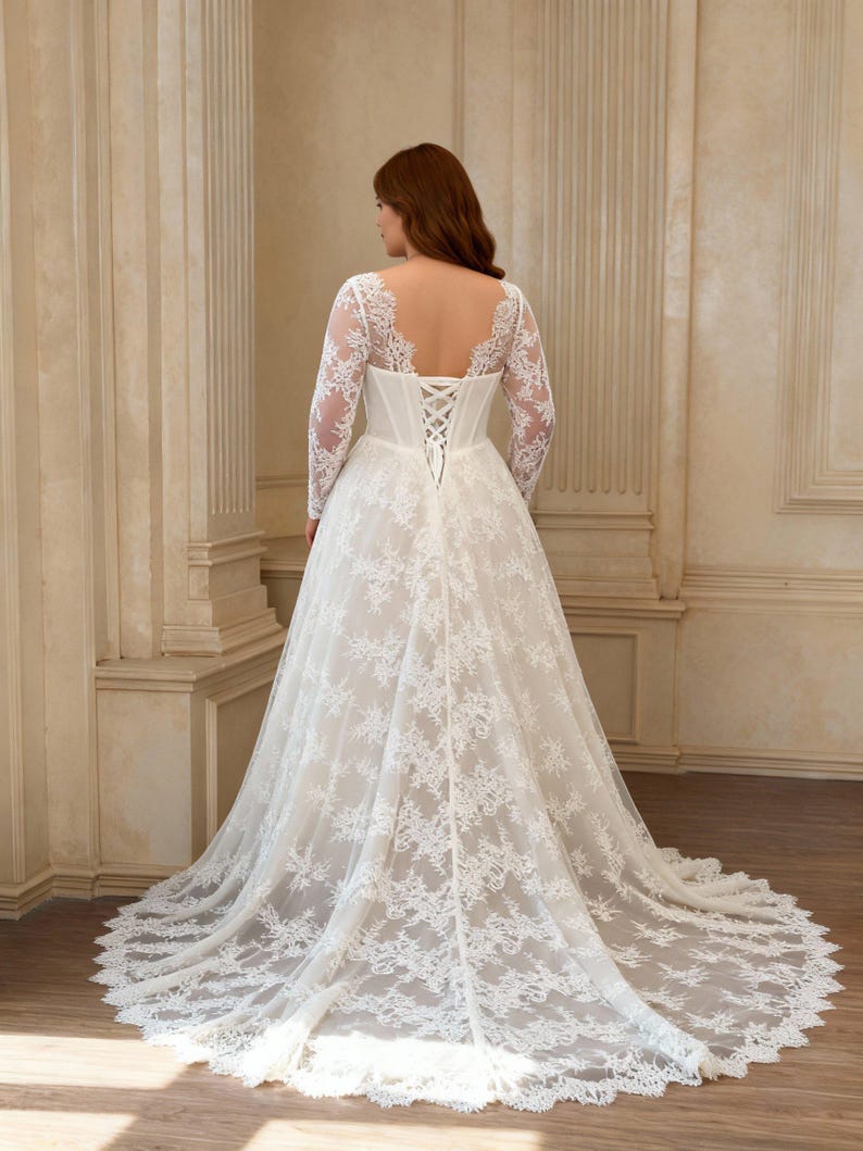 May include: A floor-length white lace gown featuring long sheer sleeves, a deep scoop back, and a corset-style bodice with crisscross lacing. The skirt is full and flows into a train, with intricate floral lace patterns covering the entire garment.