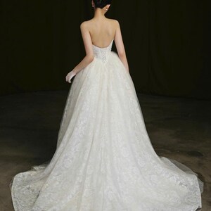 Puede incluir: Un vestido de novia blanco sin tirantes con una falda amplia y una larga cola. El vestido es de encaje y tiene un corpi&ntilde;o ajustado. El pelo de la novia est&aacute; peinado en un mo&ntilde;o.
