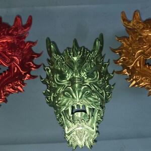 May include: Three dragon head sculptures in red, green, and gold. Each dragon head features intricate details, including sharp teeth and textured scales. The sculptures are likely decorative items or wall hangings.