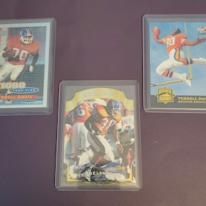 May include: Three trading cards featuring Terrell Davis, a former American football running back. The cards are in protective plastic sleeves. The cards are from the 1996 Rookie Summit, 1996 Score, and 1996 1000 Yard Club sets.