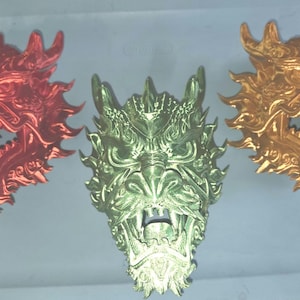 May include: Three dragon head sculptures in metallic red, metallic green, and metallic gold. Each dragon head features intricate scales, sharp horns, and an open mouth with visible teeth, showcasing a detailed, textured, and three-dimensional design.