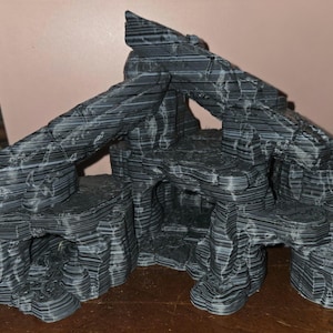 May include: A layered, dark gray and black decorative aquarium cave structure. The artificial rock formation features multiple levels, arches, and openings, creating a textured, naturalistic appearance. The design mimics a rocky landscape.
