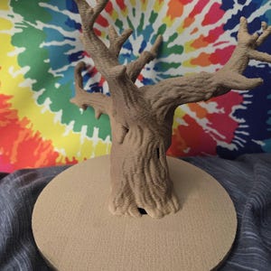 May include: A brown, textured tree sculpture with detailed branches and trunk, mounted on a circular base. The tree is set against a colorful tie-dye background, creating a striking contrast. The sculpture is a decorative item.