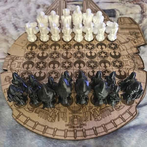 May include: A wooden Star Wars-themed chess set. The board is shaped like the Millennium Falcon, with laser-cut details. White chess pieces are on one side, and dark gray pieces on the other. The chess pieces are designed to resemble characters from the Star Wars movies.