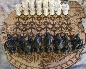 May include: A wooden Star Wars-themed chess set. The board is shaped like the Millennium Falcon, with laser-cut details. White chess pieces are on one side, and dark gray pieces on the other. The chess pieces are designed to resemble characters from the Star Wars movies.
