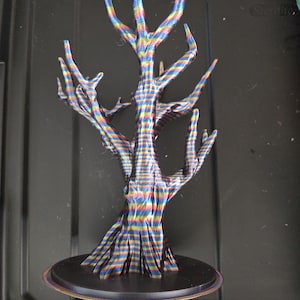 May include: A colorful, abstract tree sculpture with a black base. The tree features a striped pattern in shades of blue, red, yellow, and green. The sculpture has a textured appearance and is set against a dark background.