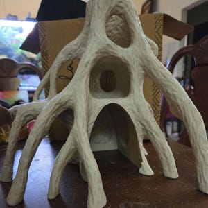 May include: A cream-colored, tree-like sculpture with multiple openings and textured surfaces. The sculpture has a root-like appearance with several branches extending outwards. The piece is likely a decorative item or a unique home accent.