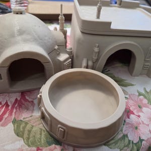May include: A set of three unpainted beige 3D printed miniature structures including a dome-shaped building with an arched entrance, a rectangular building with a flat roof and stairs, and a circular bowl-shaped container with exterior detailing.