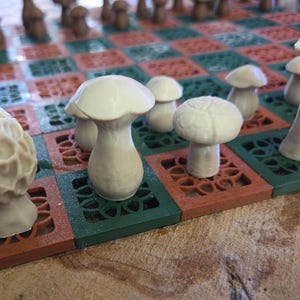 May include: A unique mushroom-themed chess set. The chess pieces are white mushroom figures, set on a board with red and green squares. The board has a decorative, openwork design. The pieces include morels and other mushroom shapes.