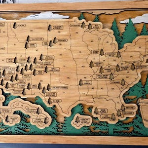 May include: Wooden relief map of the United States, featuring state outlines and national park locations. The map is framed in wood, with green painted trees and clouds adding depth. The map is a decorative piece.