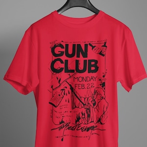 May include: Red t-shirt with a black graphic print of a band poster. The poster says "Gun Club" and "Monday Feb. 22".