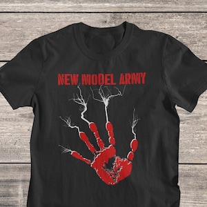 Pode incluir: Camiseta preta com uma impressão de mão vermelha e raios. O texto "NEW MODEL ARMY" está impresso em vermelho acima da impressão de mão.