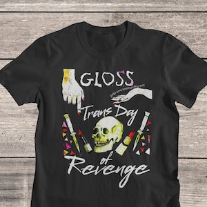 May include: Black t-shirt with a graphic design of a skull surrounded by makeup and the text "GLOSS (Girls Love Our Sweet Pretty Story) Trans Day of Revenge"