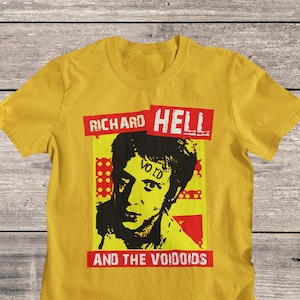 Op de afbeelding: Een geel T-shirt met een zwart-wit afbeelding van Richard Hell and the Voidoids. De tekst "Richard Hell" en "And The Voidoids" is rood. De tekst "Void" staat op het voorhoofd van de persoon.