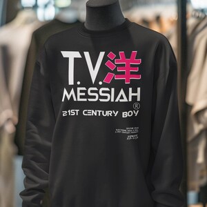 May include: Black sweatshirt with white and pink text that reads "T.V. MESSIAH" and "21ST CENTURY BOY." The sweatshirt is displayed on a mannequin in a clothing store.