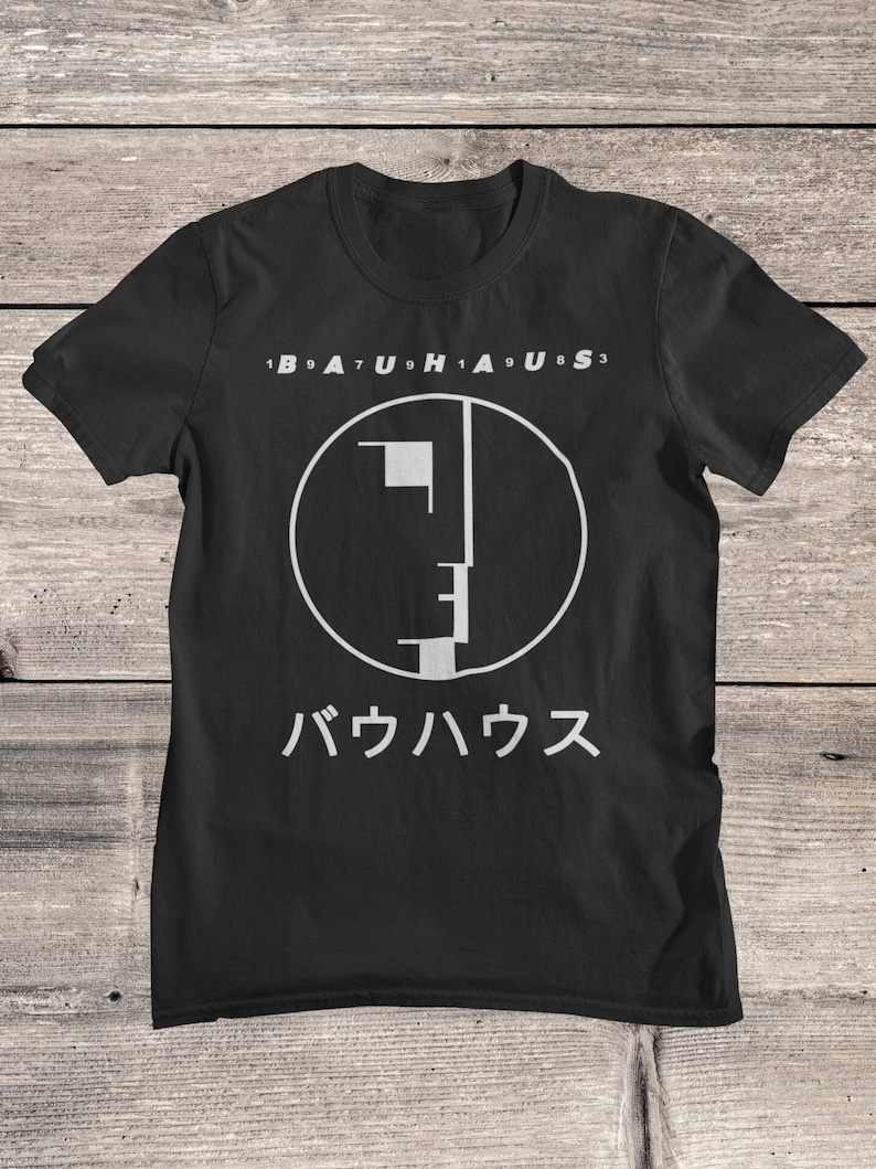 May include: Black t-shirt with a white graphic of a circle with a stylized face inside. The text "1979 Bauhaus 1983" is above the graphic and the text "バウハウス" is below the graphic.