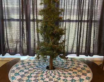 Puede incluir: Una falda de árbol de Navidad grande y acolchada con fondo blanco y un patrón de bastones de caramelo rosa, azul y verde y copos de nieve. La falda está sobre una mesa de madera con un pequeño árbol de Navidad en el centro.