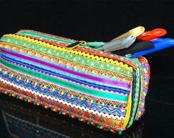 May include: A colorful pencil case with a zipper closure and a variety of colorful ribbons and tassels. The case is filled with pens and pencils.