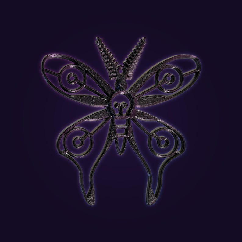 Op de afbeelding: Een donker, metaalkleurig vlinderornament met ingewikkelde uitgesneden patronen in de vleugels. Het ontwerp bevat een centraal lichaam met een detail in de vorm van een gloeilamp en twee opvallende, getextureerde antennes aan de kop.