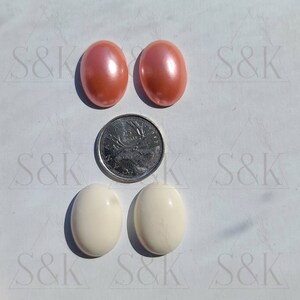 Può includere: Quattro cabochon ovali color pesca e crema, con una moneta da 25 centesimi canadese per riferimento. I cabochon hanno una superficie liscia e lucida. L'immagine è su una superficie bianca.