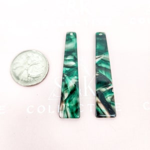 May include: Two rectangular green and white marbled acrylic earring pendants with a hole at the top. A quarter is next to the pendants for size comparison. The pendants have a glossy finish.