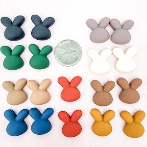 以下が含まれることがあります： 様々な色のウサギの形をした装飾品のコレクション。ダークティール、グリーン、グレー、ホワイト、タン、レッド、ブラウン、ブルー、マスタードイエローなど。サイズの比較のためにコインが配置されています。これらはおそらくクラフト用品です。