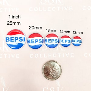 May include: A selection of round, glossy buttons featuring a red, white, and blue design with the word "BEPSI" in blue. Sizes vary from 25mm to 12mm. A coin is included for scale. The buttons are displayed on a pale pink background.