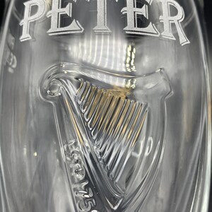 May include: A clear glass pint glass with the name "PETER" etched on the top and a harp logo with "Est. 1759" etched on the bottom.