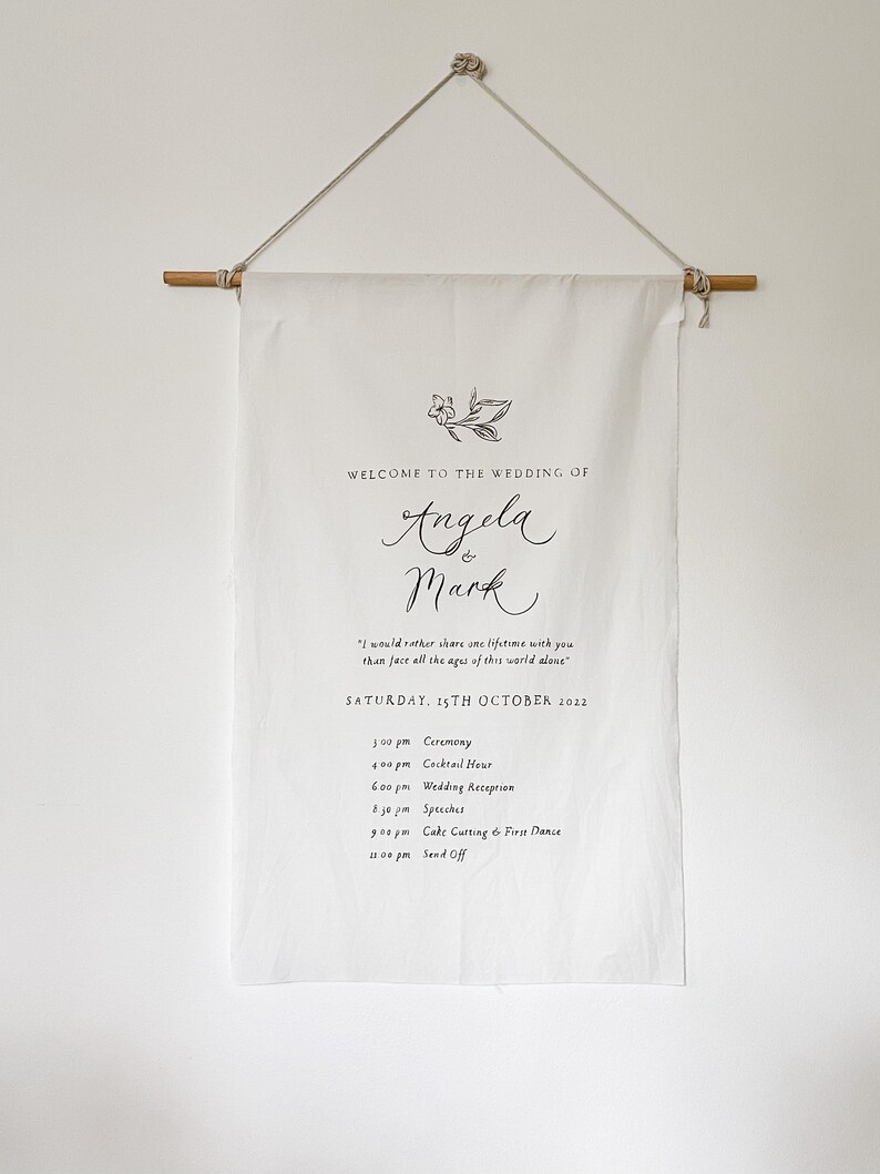 May include: White wedding banner with a floral design and the text "Welcome to the wedding of Angela & Mark". The banner also includes the wedding date, "Saturday, 15th October 2022", and a list of wedding events with times.