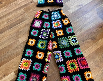 May include: A crochet top and wide-leg pants set in black with colourful square patterns. The top is a cropped style with thin straps. The pants have a high waist and are made of a soft, lightweight fabric.