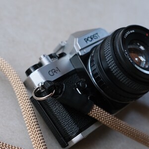 May include: A silver and black Porst CR-1 35mm film camera with a black lens and a tan camera strap. The lens is marked with "1:1.9/50 mm" and "Reflex". The camera is on a neutral background.