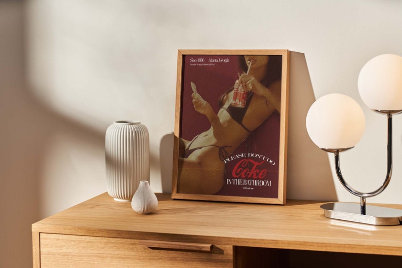 May include: A framed poster featuring a woman in a bikini drinking from a can of Coke. The poster reads "Please don't do Coke in the bathroom without me."