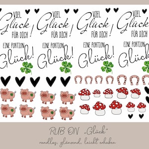 Könnte beinhalten: Eine Bogen mit Rub-on-Aufklebern mit verschiedenen Glücksbringer, darunter vierblättrige Kleeblätter, Hufeisen, Pilze und Schweine. Die Aufkleber sind mit dem Text "Viel Glück!" bedruckt.