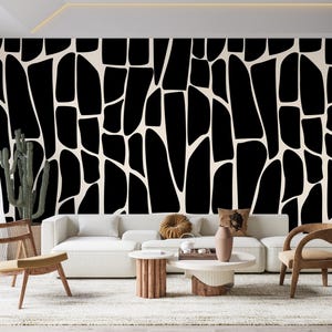 May include: A modern living room with a black and white abstract patterned wall. A white sofa, wooden chairs, and a round coffee table are in front of the wall. A cactus plant adds a touch of greenery to the room.