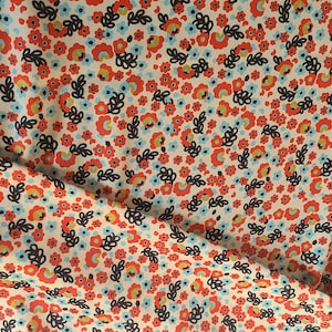 May include: A fabric with a repeating floral pattern. The design features small red, yellow, and blue flowers with dark gray leaves on a cream background. The fabric is slightly wrinkled, suggesting it is a soft material.