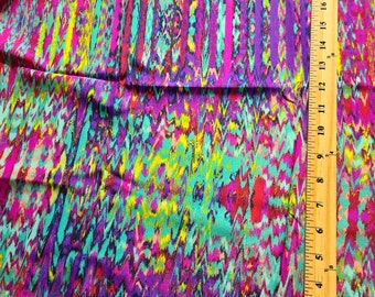 May include: A colourful fabric featuring a zigzag pattern in shades of purple, teal, pink, and yellow. A wooden ruler with inch markings is visible along the right side of the fabric, showing measurements.