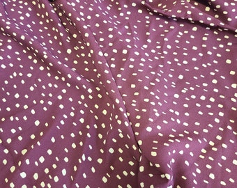 May include: Close-up of a deep purple fabric with a pattern of small, irregular white dots. The fabric is draped, showing folds and shadows. The material appears to be soft and flowing, possibly a dress or blouse.
