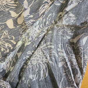 May include: A close-up of a gray and white patterned fabric with a floral design. The fabric is soft and flowing, and the pattern is subtle and elegant.