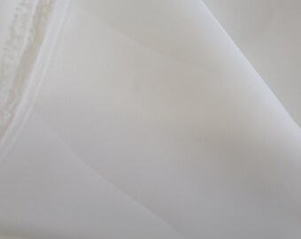 May include: Close-up of white fabric, possibly a sheer material, with visible folds and layers. The fabric appears soft and delicate, with a slightly translucent quality. The edges of the fabric are visible, suggesting it may be cut or unfinished.