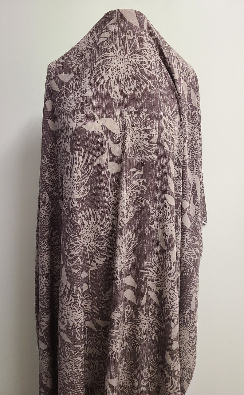 May include: A brown fabric with a white floral print. The fabric has a textured surface and a subtle sheen.