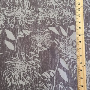 May include: A close-up of a brown fabric with a white floral pattern. The fabric has a textured, linen-like appearance. A ruler is visible in the bottom right corner of the image.