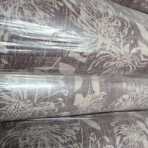 May include: Rolls of brown fabric with a white floral pattern. The fabric is wrapped in clear plastic.