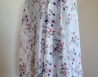 May include: White fabric with a floral pattern. The fabric features a repeating design of pink and red flowers with blue accents and green leaves. The flowers are scattered across the white background.