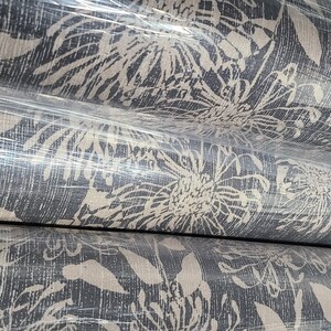 May include: Close-up of rolls of fabric with a white floral pattern on a dark gray background. The fabric is wrapped in plastic.