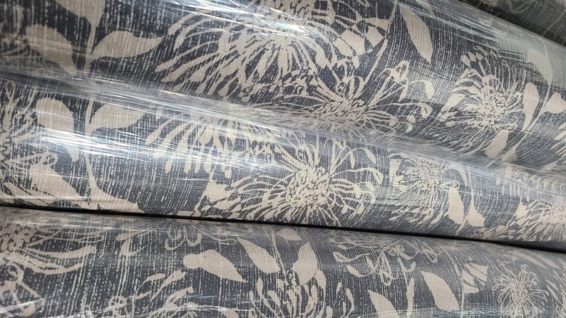 May include: Close-up of rolls of fabric with a white floral pattern on a dark gray background. The fabric is wrapped in plastic.