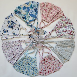 Könnte beinhalten: Set mit zehn Stoffmasken mit Blumenmustern. Die Masken sind aus Baumwolle und haben verstellbare Ohrschlaufen. Die Masken sind in verschiedenen Farben, darunter Blau, Rosa, Weiß und Grau.