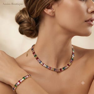 Puede incluir: Un conjunto de collar y pulsera en tono dorado que presenta una fila continua de piedras preciosas multicolores de corte baguette en tonos rojo, verde, azul, amarillo y transparente. Las piezas de joyería están unidas por una cadena y cierre.