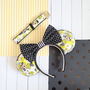 May include: Black and white polka dot bow headband with a yellow and white Minnie Mouse print on the ears. The headband is decorated with lemons and Minnie Mouse characters.