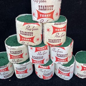May include: A collection of green rug yarn rolls labeled "Rug Yarn READICUT TERRY" in red and white packaging. The rolls are stacked, showcasing the product's texture and branding. The yarn appears to be tightly wound, suggesting a durable material for rug making.