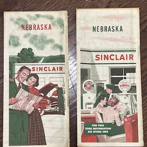 May include: Two vintage Nebraska travel brochures with Sinclair branding. The brochures feature illustrations of people with cars and maps. One brochure has the text "For Free Tour Information See Other Side."